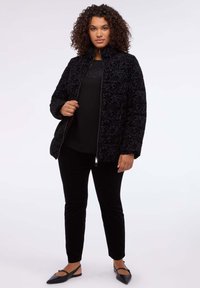 Czarna pikowana kurtka z kwiatowym wzorem, stojącym kołnierzem i zapinana na zamek. Noszona na czarnym topie i zestawiona z czarnymi welurowymi spodniami.