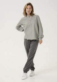 Grå langærmet top med knaplukning og løs pasform, parret med mørkegrå tapered bukser med elastiske manchetter og hvide sneakers.