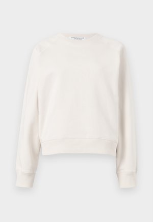 Μπεζ μακρυμάνικη μπλούζα με στρογγυλή λαιμόκοψη, με ριμπ μανσέτες και τελείωμα, εκτεθειμένη σε απλό φόντο.