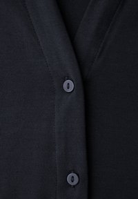 Cardigan noir avec un col en V, fabriqué dans un tissu lisse et extensible, avec une seule fermeture à bouton sombre à l'avant.