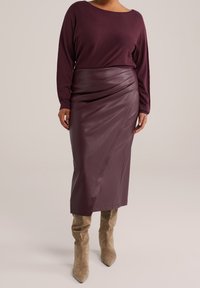 Jupe en cuir bordeaux avec un design drapé, associée à un haut à manches longues violet foncé et des bottines beiges. Texture lisse, longueur genou.