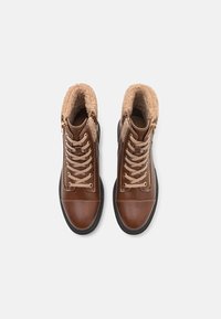 Bottines en cuir marron avec une doublure en fausse fourrure, lacets crème et zip sur le côté. Présentent un bout arrondi et une semelle en caoutchouc.