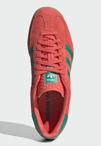 Červené semišové tenisky so zelenými pruhmi, guľatá špička, textúrovaný jazyk a polstrovaná stielka. Obsahuje logo Adidas na jazyku a podrážke.