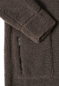 Tissu en polaire marron avec une poche zippée rectangulaire et un poignet de manche replié montrant une texture douce, épaisse et bouclée.