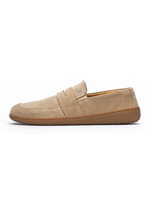 Mocasín beige de ante sin cordones con puntera redonda, costura lateral y suela de goma marrón texturizada para uso casual.