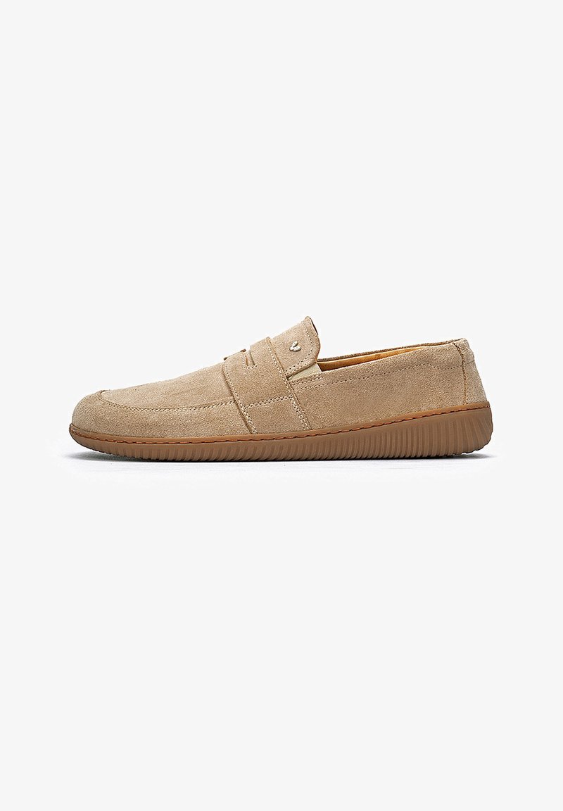 Mocasín beige de ante sin cordones con puntera redonda, costura lateral y suela de goma marrón texturizada para uso casual.