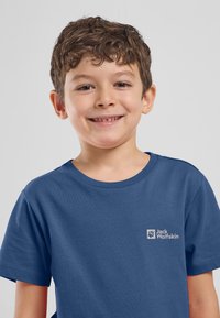 Blauwe katoenen T-shirt met korte mouwen en een ronde halslijn, met een klein wit logo op de linkerborst. Glad textuur.