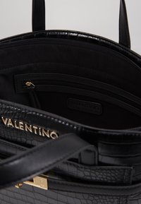 Černá kožená kabelka s texturou krokodýlího embosování, zlatými kovovými detaily a vnitřní kapsou na zip. Obsahuje detail loga uvnitř.