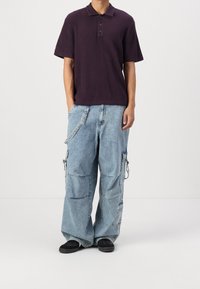 Pánské tričko s límečkem v tmavě fialové proužkované tkanině se třemi knoflíky a krátkými rukávy, v kombinaci se světle modrými volnými cargo kalhotami s mnoha kapsami.
