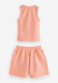 Ljust rosa bomullstopp och shorts-set. Toppen har ribbat mönster; shortsen har resår i midjan och en avslappnad passform.