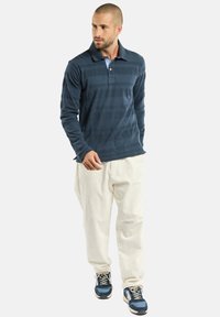Polo à manches longues bleu marine avec des rayures horizontales, col uni, associé à un pantalon beige clair et des baskets de sport bleues.