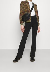 Blommönstrad bomberjacka i olivgrön, vit T-shirt, svarta ribbade byxor och svarta snörstövlar; liten svart crossbody-väska.