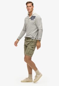 Grijze polo met lange mouwen en een witte kraag, groene cargoshorts, beige sneakers en tan sokken. Bevat logo-detail op de borst.