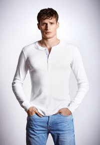 Witte lange mouwen henley shirt met een knoopsluiting bij de hals, gecombineerd met lichtblauwe spijkerbroek. De stof lijkt glad en aansluitend.