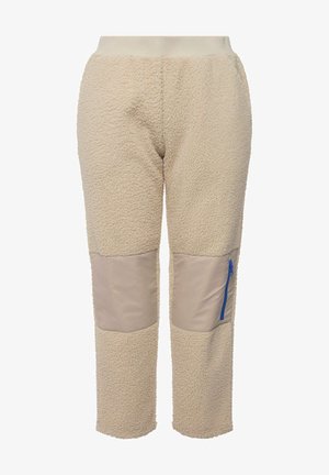 Beżowe spodnie ocieplane frotte z teksturowaną powierzchnią, z beżowymi łatami na kolanach oraz niebieską kieszenią na zamek po prawej stronie.