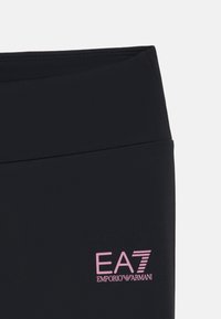 Leggings sportivi neri con una texture liscia e elastica, caratterizzati da un logo rosa EA7 Emporio Armani sulla parte inferiore della gamba sinistra.