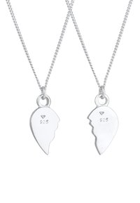 Sølvhalssmykker med hjerteformede vedhæng, som har et delt design. Hvert vedhæng er stemplet med "925" og et diamanthøjtag.