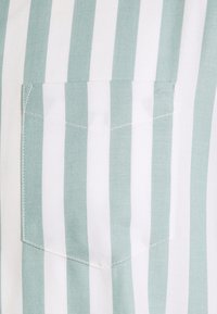 Camicia leggera in cotone con strisce verticali verde chiaro e bianche, dotata di una piccola tasca applicata e dettagli di cucitura fine.
