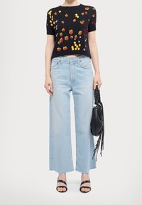 Suéter corto negro de manga corta con bordado floral, vaqueros de pierna ancha azul claro con dobladillos deshilachados y bolso negro. Sandalias negras de tiras en los pies.