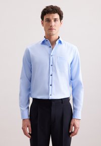 Jasnoniebieska, długorękawowa koszula z guzikowym kołnierzykiem i kieszenią na piersi; posiada ciemne guziki i gładką, lekką fakturę materiału.