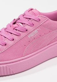 Světle růžové tenisky s texturovanou tkaninou, plochými tkaničkami a platformovou podrážkou. Mají stříbrné branding a jemné švy.