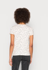Tričko s krátkým rukávem v barvě off-white, s tečkovaným vzorem černých, růžových a šedých tvarů, s kulatým výstřihem a uvolněným střihem.