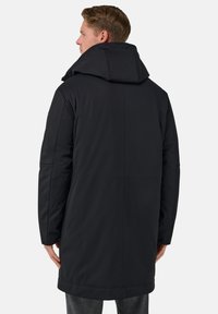 Černý prošívaný kabát s vysokým límcem a velkou kapucí. Má čistý design, hladkou texturu a délku sahající do poloviny stehen.