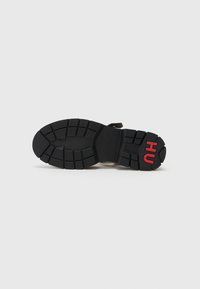 Black rubber sneaker sole with textured patterns; features a raised "HU" emblem in red. Shape is rounded with deep grooves for traction.