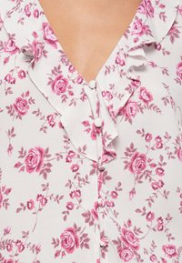Blusa floreale in tessuto leggero con motivo di rose rosa e foglie. Dotata di un colletto arricciato, dettagli con bottoni e scollo a V.