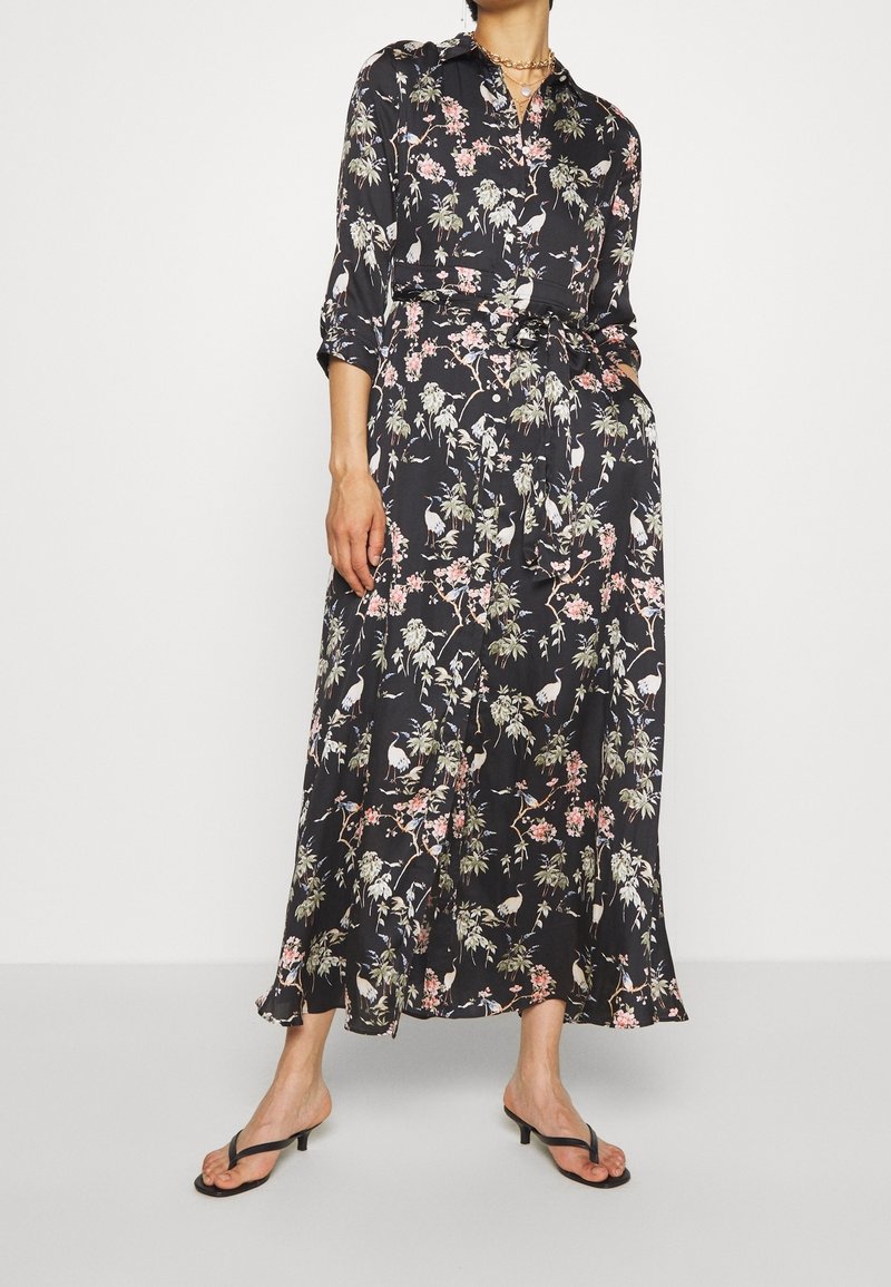 Dlouhá černá květinová šaty s límečkem, tříčtvrtečními rukávy a opaskem, zdobená růžovými květy a jeřáby.