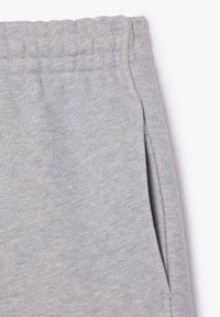 Pantalons de survêtement en tissu gris clair avec taille élastique et couture de poche latérale sur fond blanc.