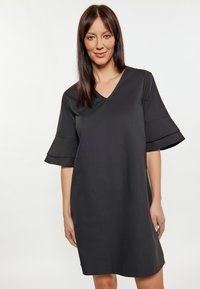 Zwarte jurk met een V-hals en uitlopende korte mouwen, gemaakt van gladde stof; kniehoogte met een losse pasvorm. Minimalistisch ontwerp zonder patronen.