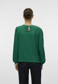 Grøn textured bluse med lange ærmer, rund halsudskæring og nøglehulåbning på ryggen. Stoffet har lodrette striber og en afslappet pasform.
