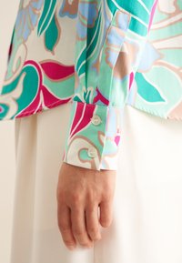Langärmlige Bluse mit buntem Blumenmuster in den Farben Teal, Pink und Beige; verfügt über Manschetten mit zwei Knöpfen und eine glatte Textur.