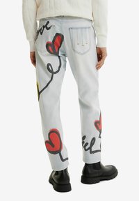 Ljusblå denimjeans med röda och svarta abstrakta hjärt-mönster, med avslappnad passform och femficksstil. Svarta gummisula stövlar.