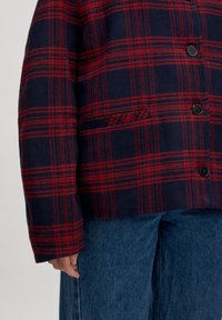 Wollen blended, marineblau en rood geruite jas met een knoopsluiting aan de voorkant, een enkele zak en brede mouwen, gecombineerd met blauwe denim broek.