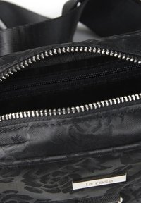 Svart nylonaxelväska med ett texturerat blommönster, dubbla dragkedjefack och en logoplatta i silverton.