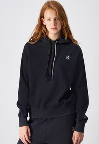 Sudadera negra con cordones y borlas, logo en el frontal y puños de canalé. Corte relajado y material suave para mayor comodidad.