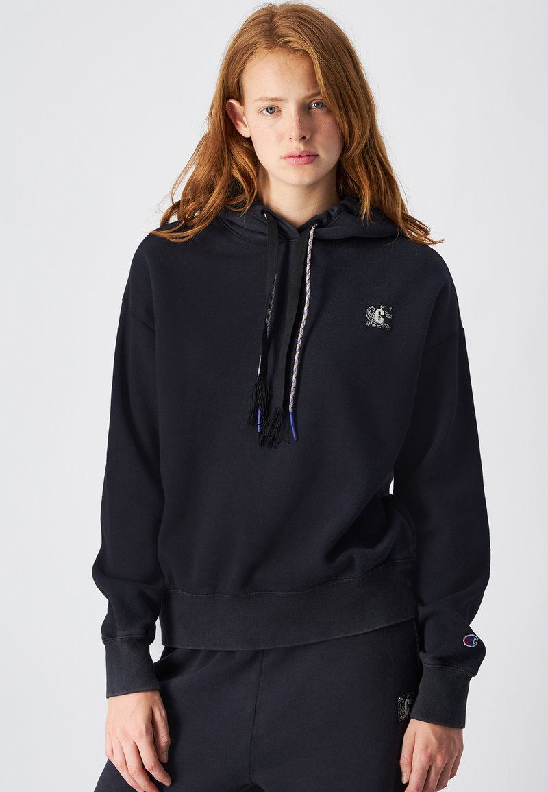 Sudadera negra con cordones y borlas, logo en el frontal y puños de canalé. Corte relajado y material suave para mayor comodidad.