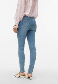 Šviesiai mėlynos spalvos siauri džinsai su vidutinio aukščio liemeniu, subtiliomis galinėmis kišenėmis ir suplaikytais kraštais, derinami su kremine spalva aukštakulniais.