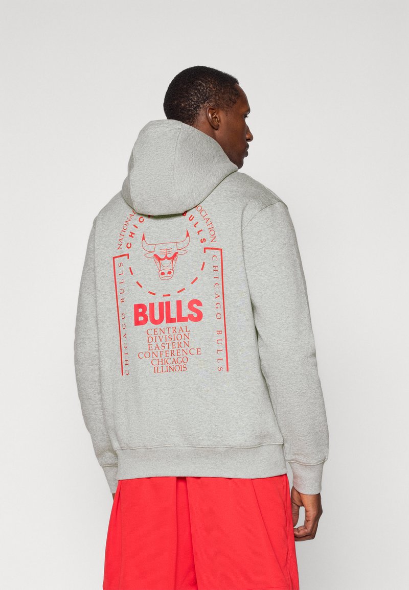 Grå hættetrøje med et rygdesign, der har en rød grafik af en tyr og tekst, der henviser til "Chicago Bulls" og detaljer om basketballdivisionen.