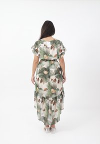 Abito maxi floreale in tessuto leggero con foglie verdi e accenti marroni, caratterizzato da un design a strati e maniche corte arricciate. Etichetta visibile sul retro.