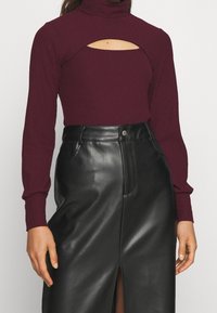 Burgundy ribbad polokrage topp med en urtagning vid bröstet, i kombination med en högmidjad svart läderkjol med en slits fram.