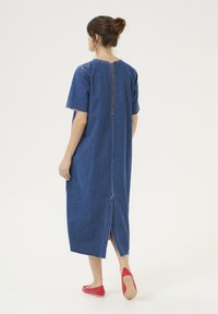 Denim obleka, srednje dolžine, z igralnimi kratkimi rokavi in robovi brez obdelave. Zadrga na hrbtu in stranska razpoka. Oblečena z rdečimi baletkami.