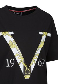 Zwarte katoenen t-shirt met een grote witte en gouden "V" graphic met bloemaccenten en de cijfers "1969" eronder. Korte mouwen, ronde halslijn.