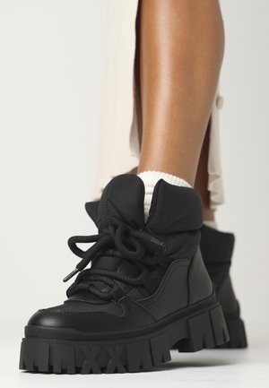 Black ankle boots made of leather and fabric, featuring a thick, textured sole, laces, and a padded collar for comfort.