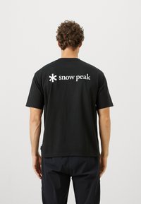 Black cotton t-shirt with short sleeves, crew neck, and a white "snow peak" logo on the back. Smooth texture, relaxed fit.