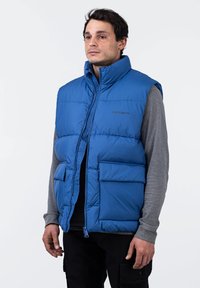 Chaleco acolchado azul con cuello alto, cremallera frontal y dos grandes bolsillos con solapa. Fabricado en material acolchado con una textura suave.