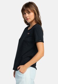 Kortærmet sort T-shirt lavet af blødt stof, med rund halsudskæring og et lille rødt logo på brystet, samt op-rullede ærmer.