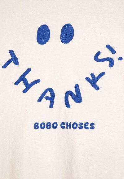 Camiseta de algodón blanca con un texto azul llamativo que dice "¡GRACIAS!" en letras redondeadas y una carita sonriente, impreso en una tipografía juguetona.